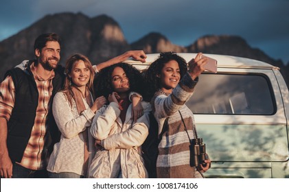 Group Of Mixed Race Friends Taking A Selfie Near The Van. Young Man And Women Together On Road Trip Making Selfie.