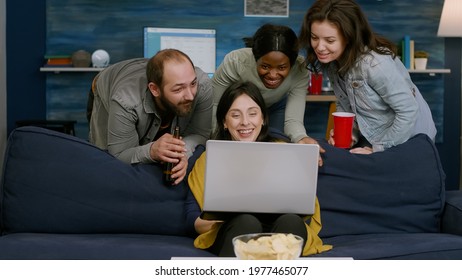 Group Of Mixed Race People Chilling On Couch Looking At Laptop Computer Watching At Entertainment Movie. Multiracial Friends Hanging Out Together Late At Night In Living Room