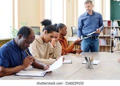 Group Of Modern Black Immigrants Attending Classes Sitting At Table Finishing Doing English Grammar Test