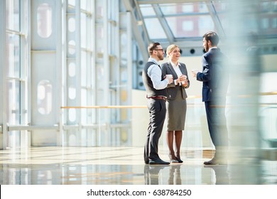 Group of modern business people chatting during coffee break  standing in sunlit glass hall of office building - Powered by Shutterstock