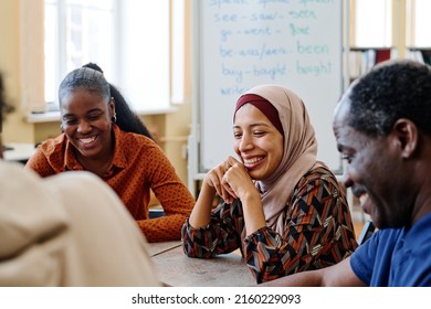 Group of modern immigrants sitting at table having fun laughing at something funny during english lesson