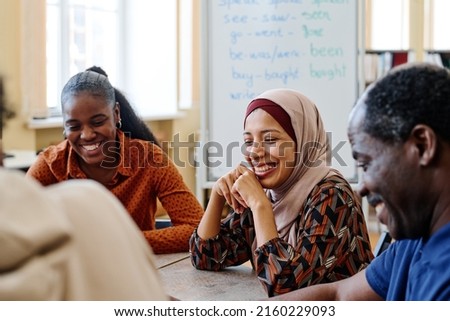 Group of modern immigrants sitting at table having fun laughing at something funny during english lesson