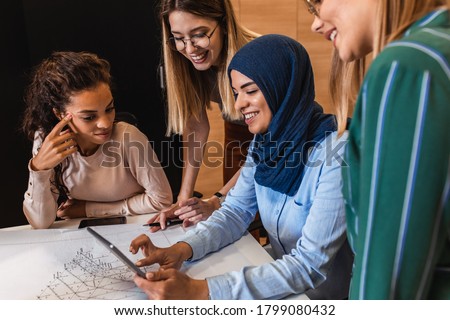 Group of modern multicultural young business women in casual wear discussing architectural designs in the creative office.