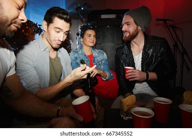 Group Of Modern Young People Chatting, Drinking Beer And Having Fun  At Late Night Party