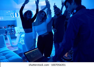 Group Of Modern Young People Dancing Listening To DJ Playing Music At Private House Party, Lit By Blue Light