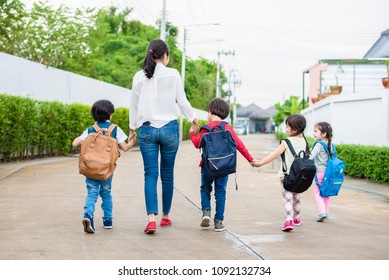 Group Of Mother And Kids Holding Hands Going To School With Schoolbag. Mom Bring Children Walk To School By Bus Together With Satchel. Back To School And Education Preschool. Parents Son Sister Family