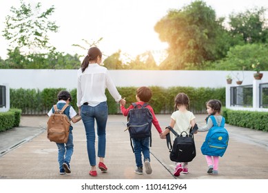 Group Of Mother And Kids Holding Hands Going To School With Schoolbag. Mom Bring Children Walk To School By Bus Together With Satchel. Back To School And Education Preschool. Parents Son Sister Family