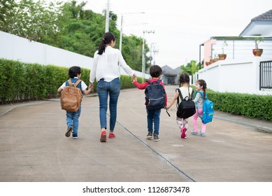 Group Of Mother And Kids Holding Hands Going To School With Schoolbag. Mom Bring Children Walk To School By Bus Together With Satchel. Back To School And Education Preschool. Parents Son Sister Family