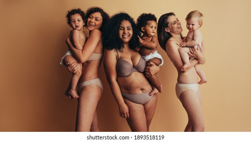 Group of mothers with babies. Women with postpartum bodies carrying their children looking at camera and smiling.