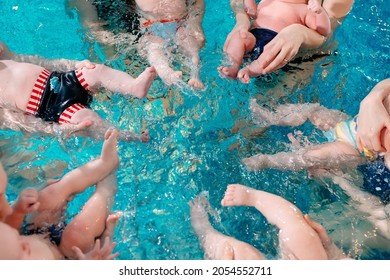 A group of mothers with their young children in a children's swimming class with a coach