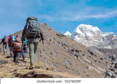 Group of Mountain Climbers walking up on yellow steep Footpath carrying large expedition Backpacks