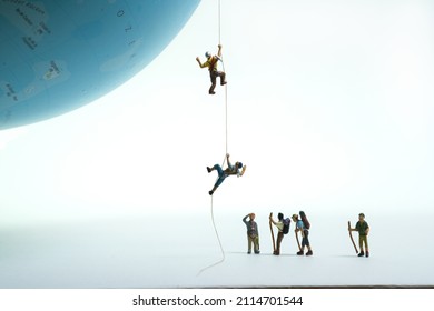 a group of mountaineers watches climbers pulling themselves up on a globe with a rope. - Shutterstock ID 2114701544