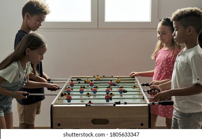 Group Of Multi Cultural Cute Children Stand Indoor Spend Playtime With Friends Playing Foosball Together. Tabletop Version Of Soccer Lovers. Having Fun And Recreation Of Alpha Generation Kids Concept