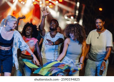 Group of multi ethnic friends dancing and waving a rainbow flag at an outdoor music festival, enjoying the live music and the vibrant atmosphere under the stage lights