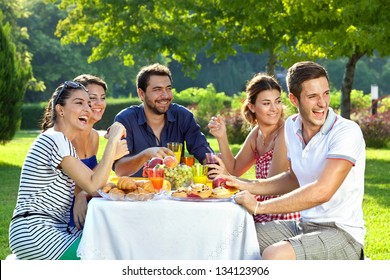 Group Of Multi Ethnic Friends Having Picnic. Group Of Adult Family Members Laughing Heartily As They Look Over Their Shoulders At Something Off Screen To The Right