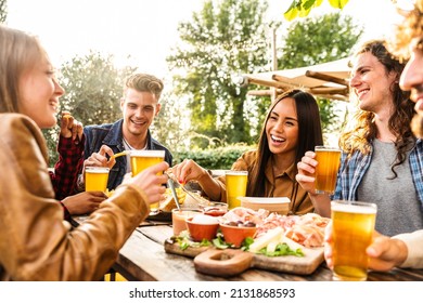 Group of multi ethnic friends having backyard dinner party together -  Diverse young people sitting at bar table toasting beer glasses in brewery pub garden - Happy hour, lunch break and youth concept - Shutterstock ID 2131868593