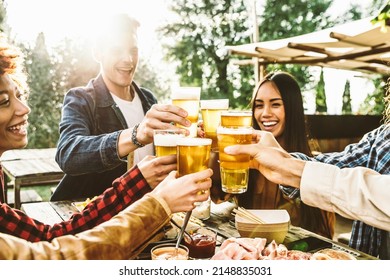 Group of multi ethnic friends having backyard dinner party together - Diverse young people sitting at bar table toasting beer glasses in brewery pub garden - Happy hour, lunch break and youth concept