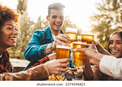 Group of multi ethnic friends having backyard dinner party together - Diverse young people sitting at bar table toasting beer glasses in brewery pub garden - Happy hour, lunch break and youth concept - Powered by Shutterstock