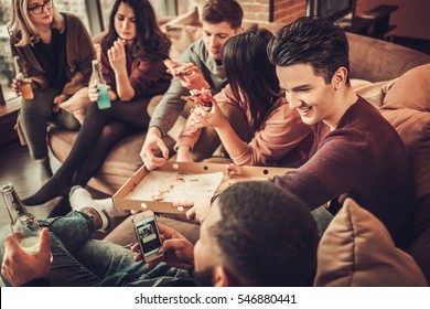 Group Of Multi Ethnic Young Friends Eating Pizza In Home Interior