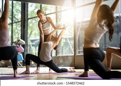 Group of multi ethnics people learning Yoga class in fitness club. Female Caucasian instructor coaching and adjust correct pose to Asian girl student at front while others doing follow them. - Powered by Shutterstock