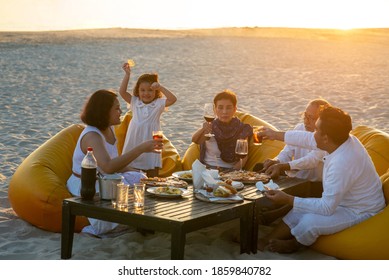 Group Of Multi Generation Asian Family Enjoy Dinner Party On The Beach At Sunset. Diverse Family With Child Girl, Adult And Senior Couple Relax And Having Fun Together On Summer Holiday Vacation