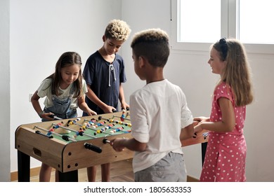 Group Of Multi National Cute Children Stand Indoor Spend Playtime With Friends Playing Foosball Together. Tabletop Version Of Soccer Lovers. Having Fun And Recreation Of Alpha Generation Kids Concept