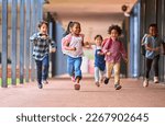 Group Of Multi-Cultural Elementary School Pupils Running Along Walkway Outdoors At School