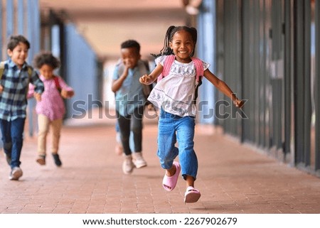 Group Of Multi-Cultural Elementary School Pupils Running Along Walkway Outdoors At School