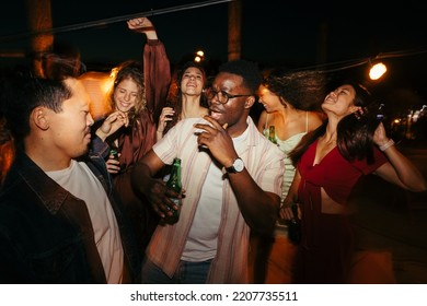 A group of multicultural friends is having a good time, dancing and drinking beer at the music festival at night. - Powered by Shutterstock