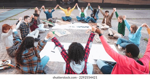 A group of multicultural peacefully activists are sitting with posters outside while holding hand by hand demonstrate against climate change - Global warming, pollution and climate change concept - Shutterstock ID 2292554421