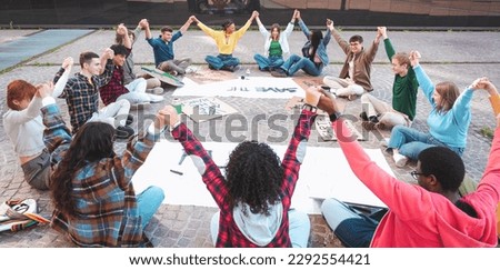 A group of multicultural peacefully activists are sitting with posters outside while holding hand by hand demonstrate against climate change - Global warming, pollution and climate change concept