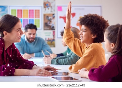 Group Of Multi-Cultural Students With Teachers In Classroom Putting Hand Up To Answer Question