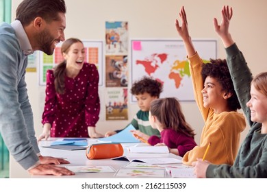 Group Of Multi-Cultural Students With Teachers In Classroom Putting Hand Up To Answer Question