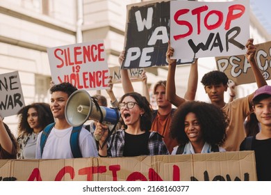 Group of multicultural teenage activists protesting against war and violence in the city streets. Generation Z demonstrators shouting slogans and raising banners while marching for world peace.