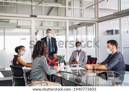 Group of multiethnic business people in meeting wearing face mask in conference room during covid19 pandemic. Business workers discussing strategy while wearing masks and keeping social distancing.