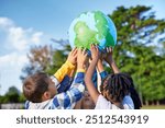 Group of multiethnic children holding model of earth in park with copy space. Primary students holding a big handmade earth model and raising it high. Save the planet, earth day and global peace.