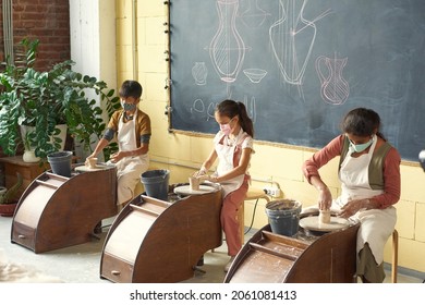 Group of multi-ethnic children in masks and aprons making clay vases using pottery wheels in workshop - Powered by Shutterstock