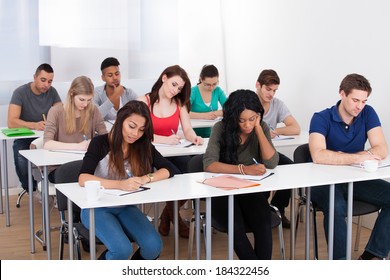 Group Of Multiethnic College Students Writing At Desk In Classroom