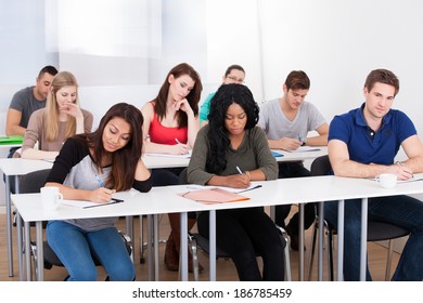 Group Of Multiethnic College Students Writing At Desk In Classroom