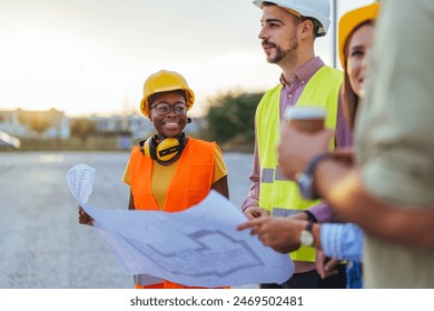 A group of multi-ethnic construction professionals, clad in safety gear and hard hats, actively review building plans outdoors. - Powered by Shutterstock