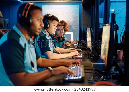 Group of multi-ethnic cybersport players in headsets sitting in front of computers and playing video games online in computer club