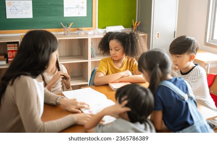 Group of Multi-ethnic elementary school and Female Asian teacher sitting on chairs in circle around and listen to her tell stories in classroom. Education, elementary school, Back to school concept - Shutterstock ID 2365786389