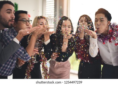 Group Of Multiethnic Friends Celebrating Christmas New Year Party , Enjoy Throwing And Blowing Confetti In An Office After Work