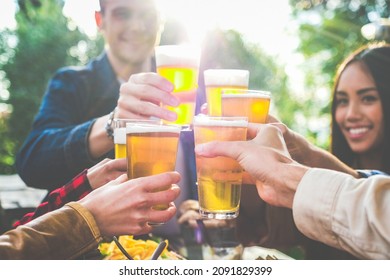 Group of multiethnic friends drinking beer at outdoor pub restaurant - Young people enjoying drinks during happy hour at terrace bar toasting with beers and chatting - Friendship concept