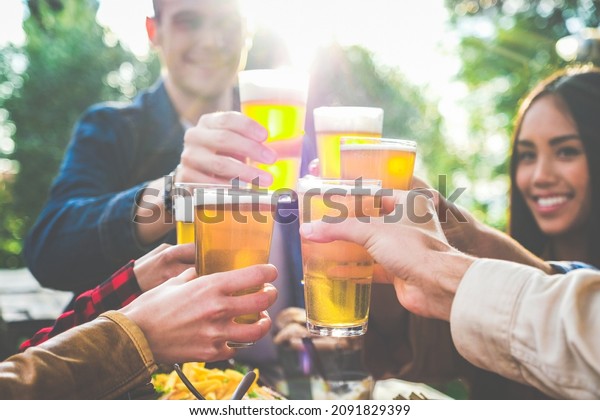 Group of multiethnic friends drinking beer at\
outdoor pub restaurant - Young people enjoying drinks during happy\
hour at terrace bar toasting with beers and chatting - Friendship\
concept