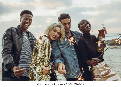 Group of multi-ethnic friends enjoying at beach with sparklers. Young men and women having fun with fireworks at the sea shore. - Powered by Shutterstock