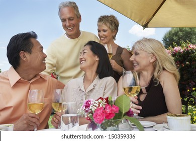 Group of multiethnic friends enjoying drinks at dinner table outdoors