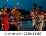 Group of multiethnic friends enjoying their party next to the pool, dancing and using sprinkles after dinner