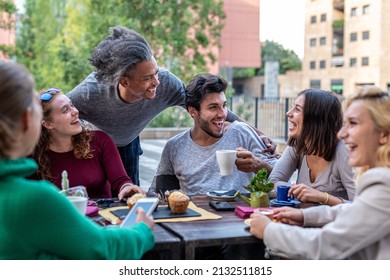 group of multiethnic friends having breakfast with coffee, cappuccino and chocolate muffin, meeting of young people outdoors at a coffee shop - Powered by Shutterstock