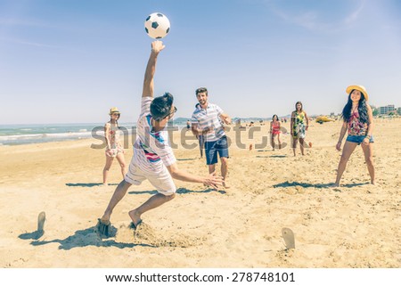 Group of multiethnic friends playing soccer on the beach - Football match on the sand on summertime - Tourists having fun on vacation with beach games
